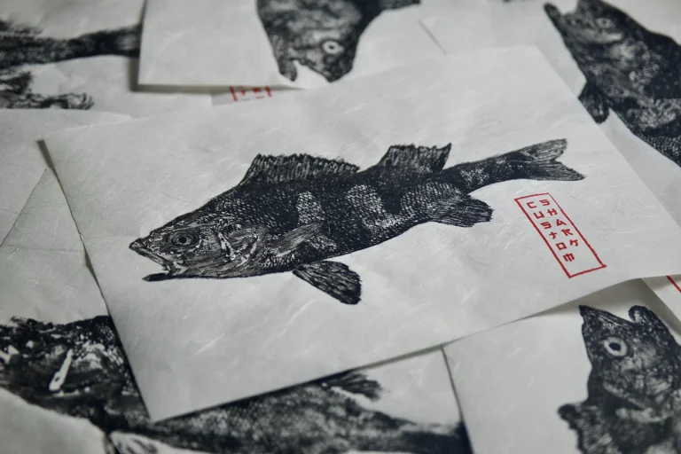 Czarna odbitka ryby z czerwoną pieczęcią Custom Shark na tle innych grafik gyotaku.